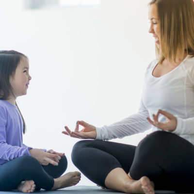 A single mother and her elementary age daughter are meditating together at home.